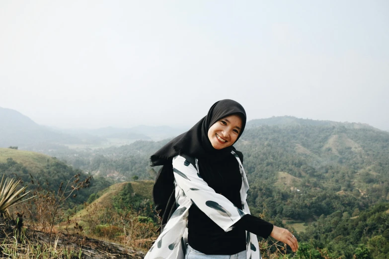 a woman standing on top of a lush green hillside, inspired by Nazmi Ziya Güran, pexels contest winner, hurufiyya, smileing nright, with black, grey, batik
