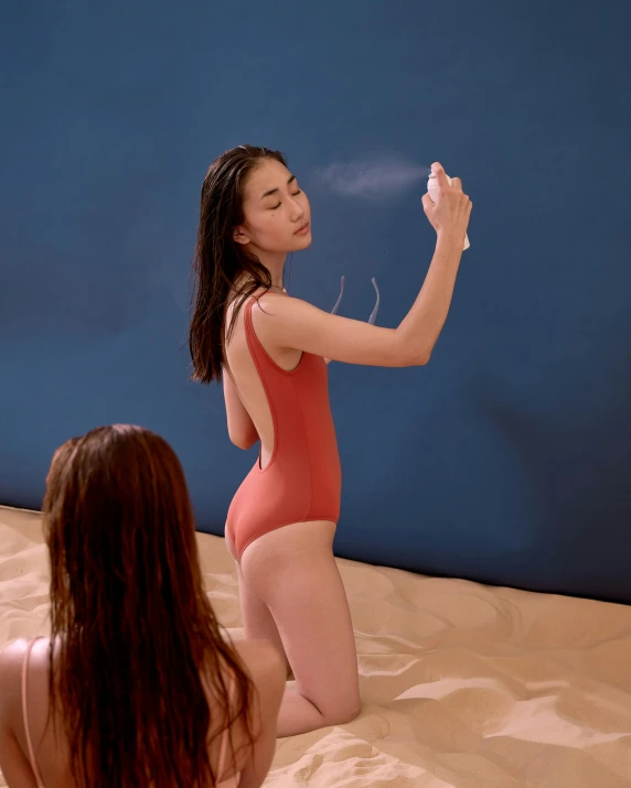 a woman sitting on top of a sandy beach, inspired by Ren Hang, unsplash, red body suit, standing in front of a mirror, pointing, low quality photo