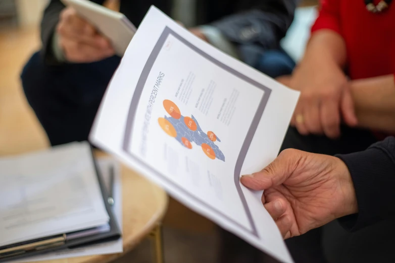 a close up of a person holding a piece of paper, infographics, people sitting at tables, colour print, easygoing