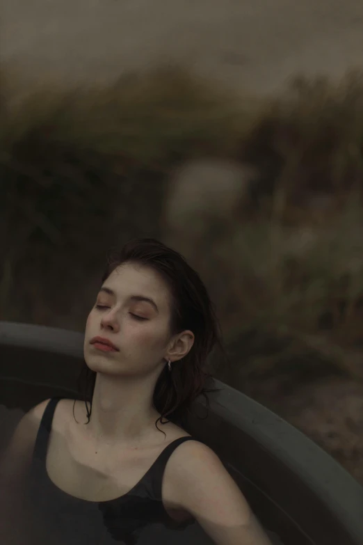 a woman sitting in a bathtub with her eyes closed, inspired by Elsa Bleda, pexels contest winner, very pale skin, on a hill, tar pit, grainy movie still