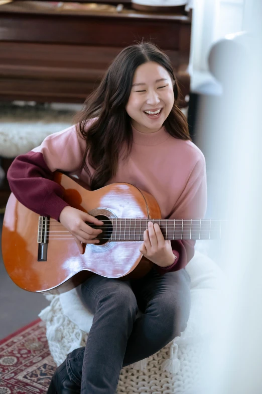 a woman sitting on a chair playing a guitar, inspired by Kim Jeong-hui, pexels contest winner, happening, square, young asian girl, sweater, welcoming smile