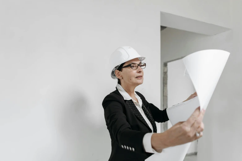 a woman in a hard hat holding a piece of paper, looking around a corner, profile image, architecture photo, image