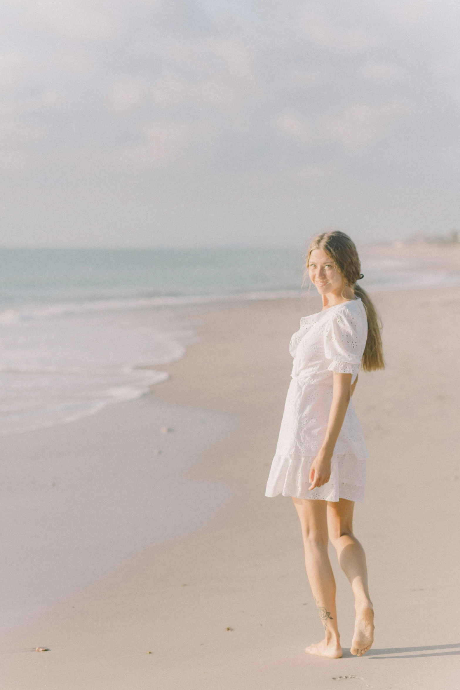 a woman standing on a beach next to the ocean, wearing a cute white dress, cinematic shot ar 9:16 -n 6 -g, soft light 8 k, view(full body + zoomed out)