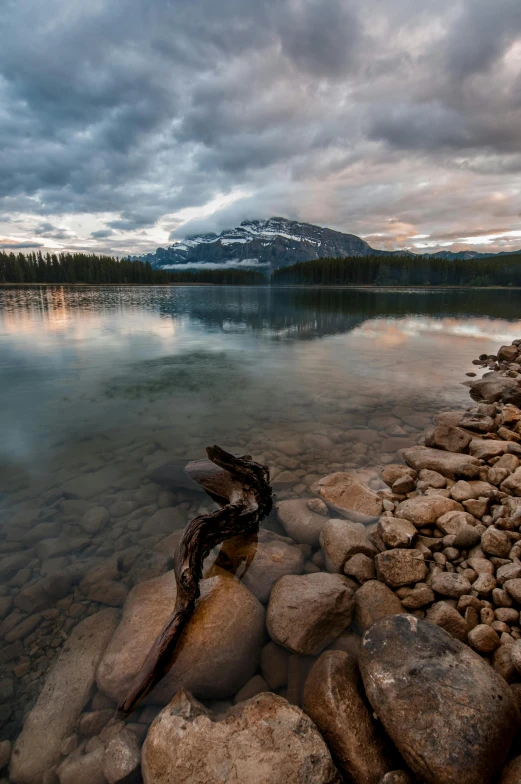 a body of water surrounded by rocks under a cloudy sky, by Raymond Normand, banff national park, sundown, 4k -, f/2