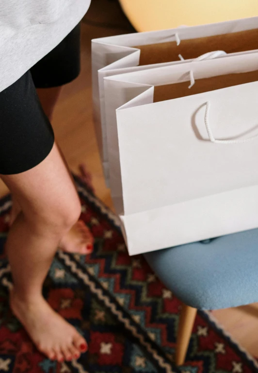 a woman holding a white shopping bag on top of a blue chair, by Julia Pishtar, pexels contest winner, sport bra and dark blue shorts, leaving a room, on high-quality paper, sustainable materials