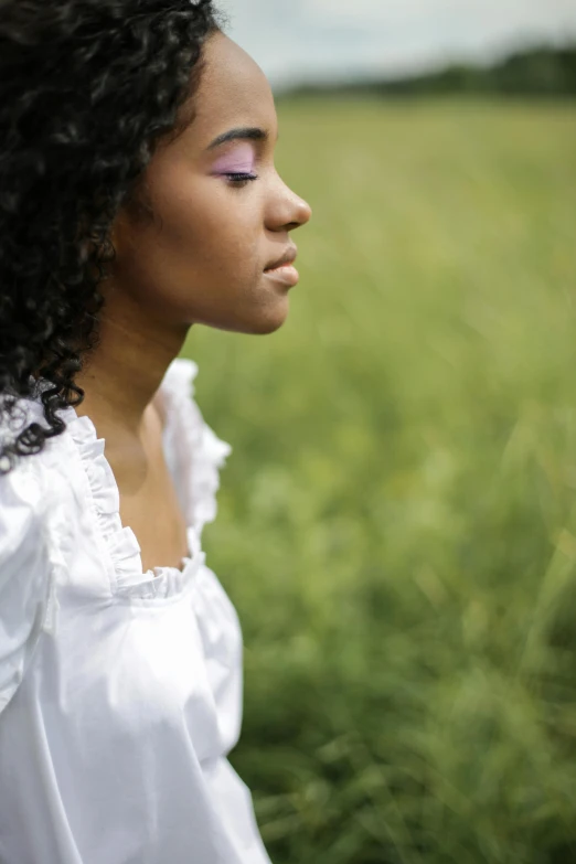 a woman with curly hair standing in a field, a picture, contemplative, wearing a white shirt, african american young woman, head bowed slightly