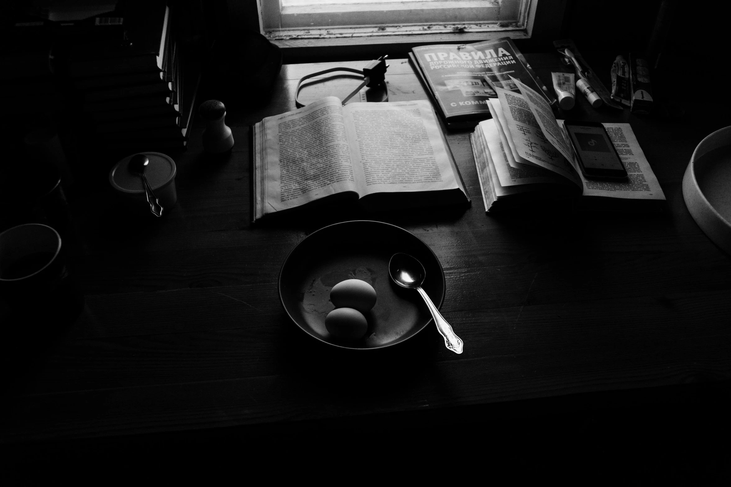 an open book sitting on top of a wooden table, a black and white photo, purism, eggs, bowl filled with food, dark image, end of the day