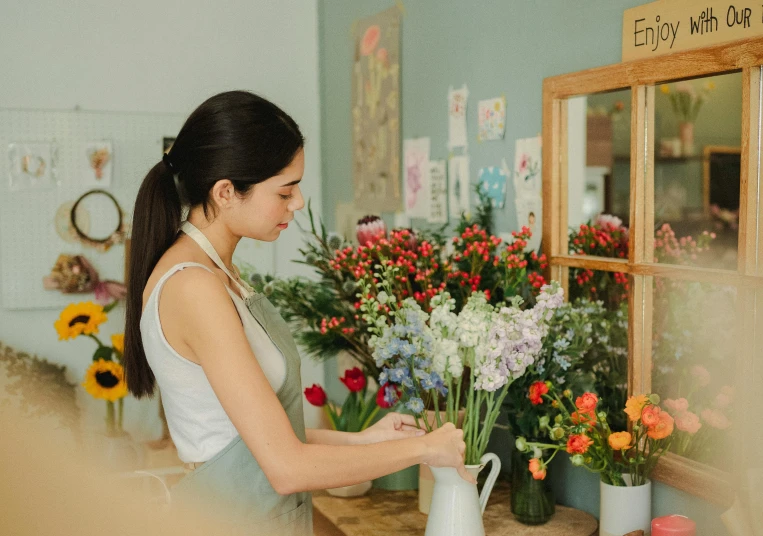 a woman is arranging flowers in a vase, pexels contest winner, shop front, looking from side, artist wearing overalls, pristine and clean design