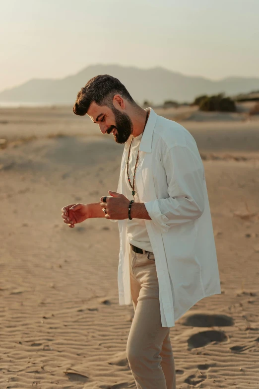 a man standing on top of a sandy beach, an album cover, trending on pexels, romanticism, bearded beautiful man, foxish guy in a lab coat, khakis, middle eastern