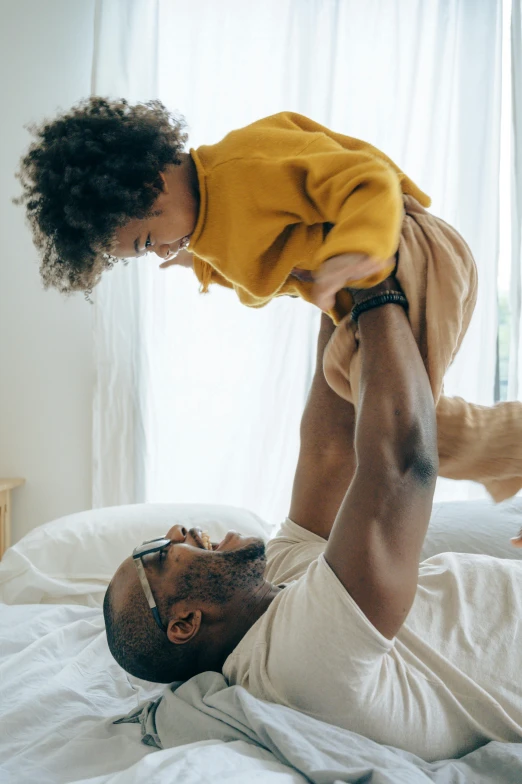 a man holding a small child on top of a bed, a stock photo, pexels contest winner, african american, kids playing, his arms spread, high textured