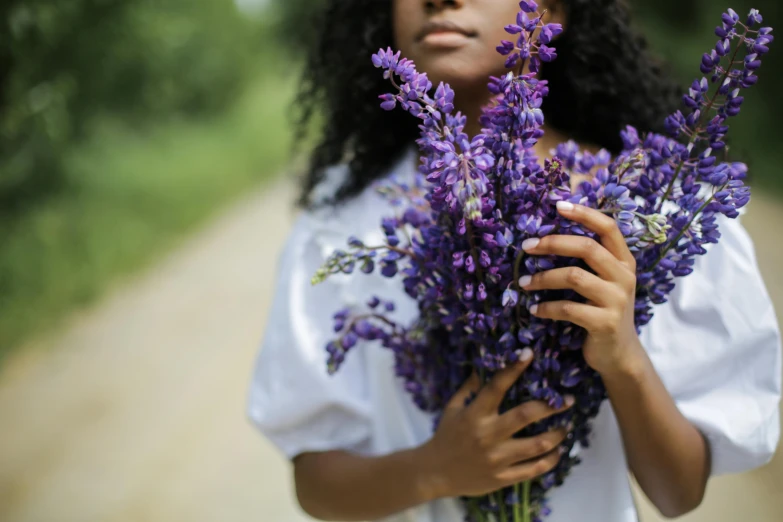 a woman holding a bunch of purple flowers, by Carey Morris, pexels contest winner, black young woman, salvia, ((purple)), cottagecore