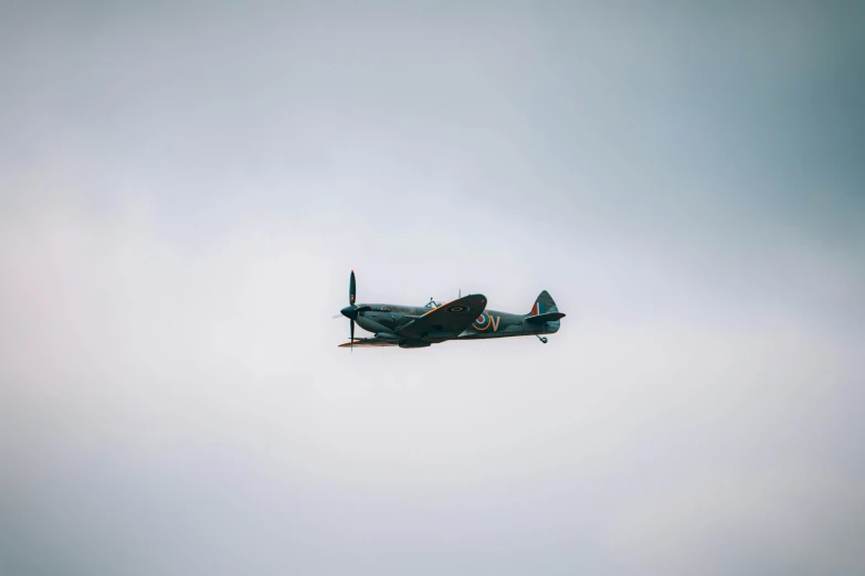 a small airplane flying through a cloudy sky, a colorized photo, by IAN SPRIGGS, pexels contest winner, spitfire, minimalist photo, military, tourist photo