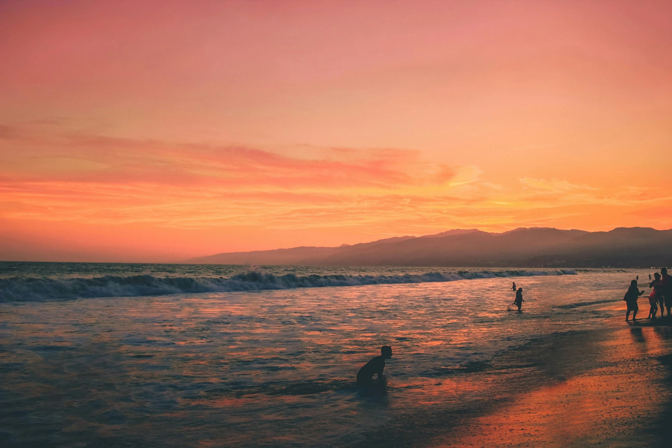 a group of people standing on top of a beach next to the ocean, unsplash contest winner, romanticism, orange and red sky, the city of santa barbara, people swimming, kids playing at the beach