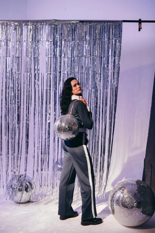 a woman standing in front of a disco ball, off - white collection, with black hair, tuxedo, wearing a purple sweatsuit