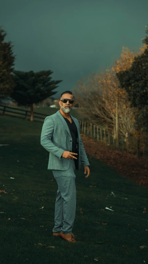 a man in a suit and sunglasses standing on a road, an album cover, inspired by Paul Henry, pexels contest winner, renaissance, gray beard, sultan, casual pose, standing outside a house