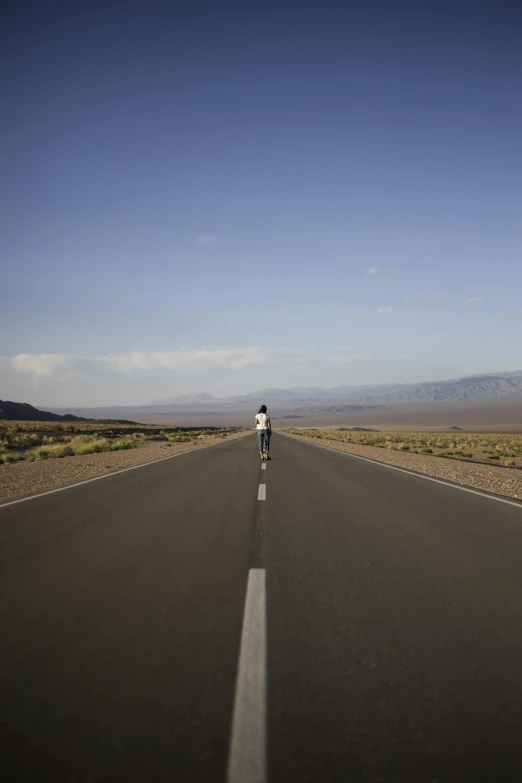 a person riding a bike down the middle of a road, inspired by Scarlett Hooft Graafland, unsplash, death valley, square, brett amory, wide open city ”