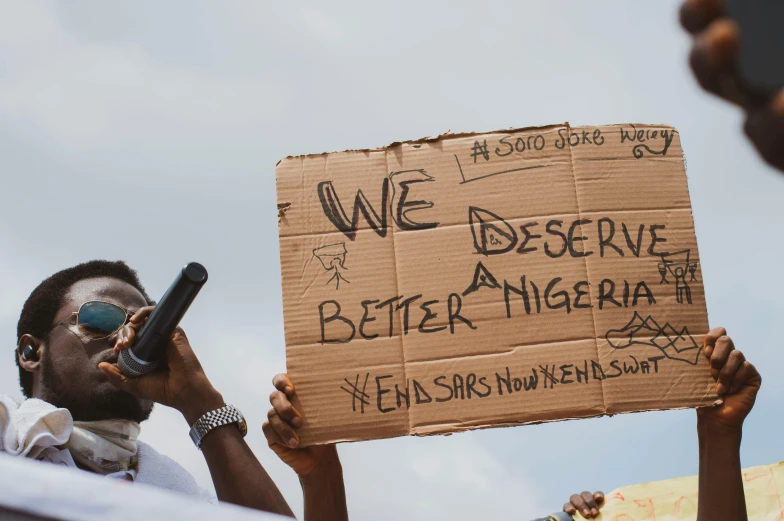 a man holding a sign that says we deserve better nigeria, pexels, excessivism, tear gas, young thug, thumbnail, cas