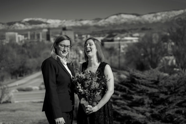 a couple of women standing next to each other, a black and white photo, unsplash, flowers in background, corporate portait, hills in the background, background image