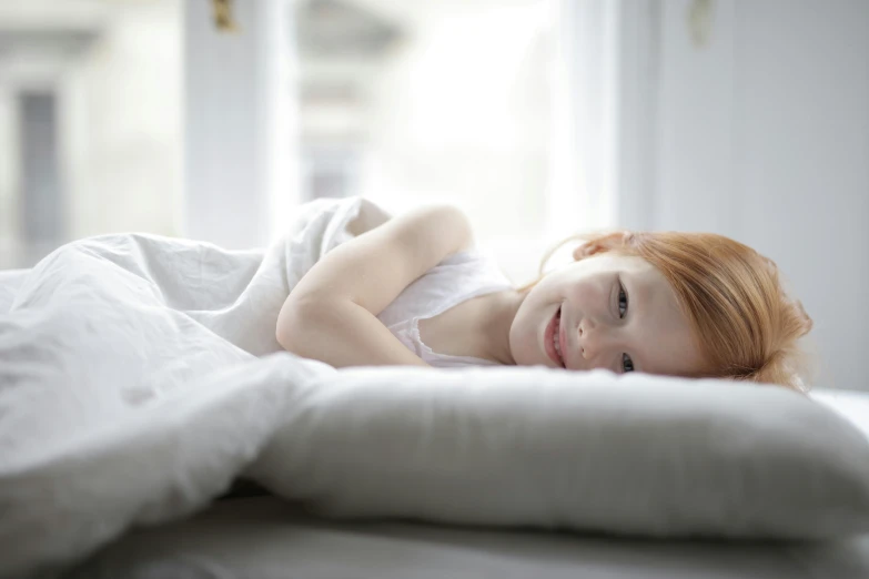 a little girl laying on top of a bed, unsplash, young redhead girl in motion, soft white glow, next gen, product introduction photo