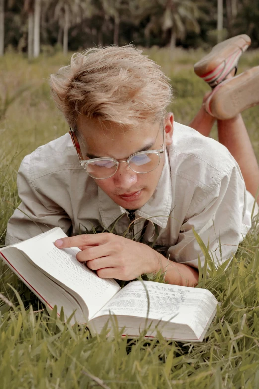 a boy laying in the grass reading a book, inspired by Oskar Lüthy, blonde guy, wearing eyeglasses, still from film, preppy style