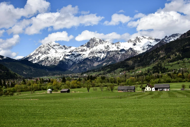 a green field with snow capped mountains in the background, by Jozef Simmler, pexels contest winner, alpine architecture, thumbnail, multiple stories, amanda lilleston