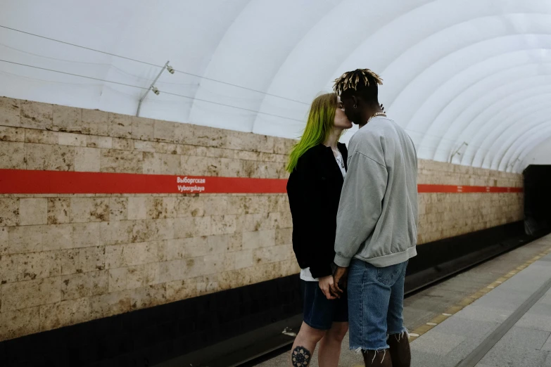 a man and a woman standing next to each other, a photo, by Attila Meszlenyi, pexels contest winner, subway station, lesbian kiss, 😭🤮 💔, mix of ethnicities and genders