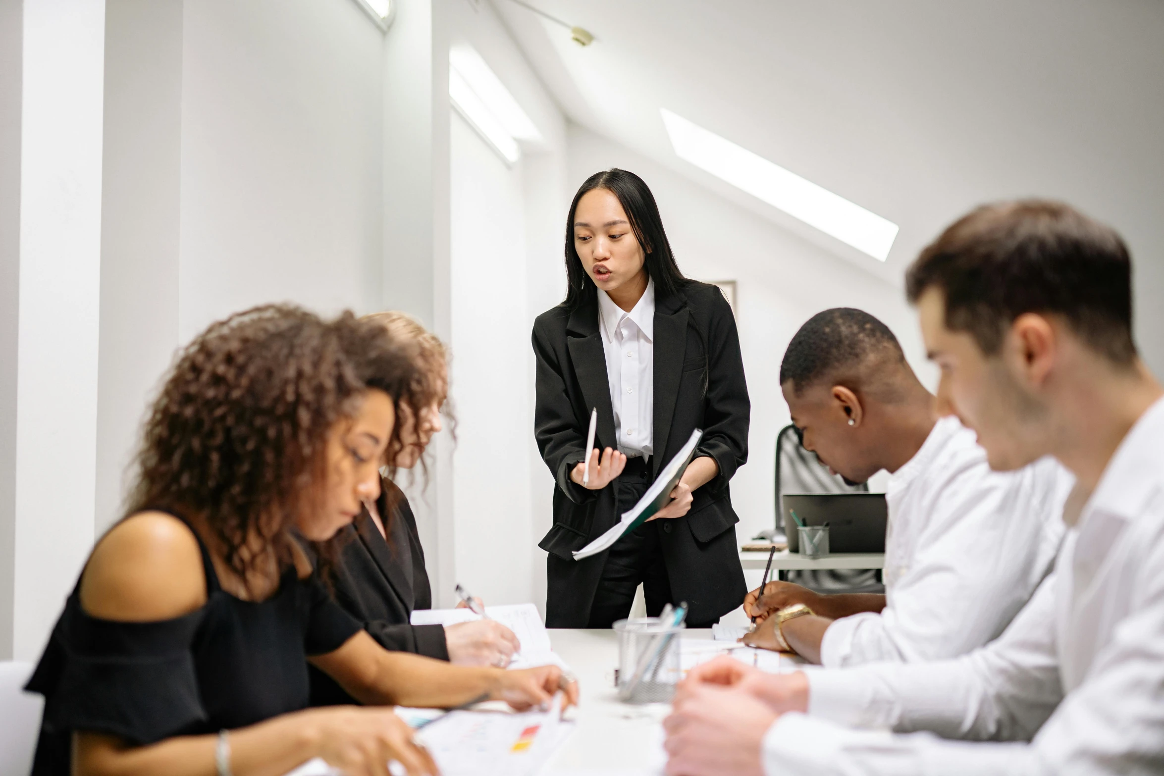 a group of people sitting around a table, by Gavin Hamilton, pexels contest winner, academic art, woman in black business suit, standing in class, asian descent, on a white table