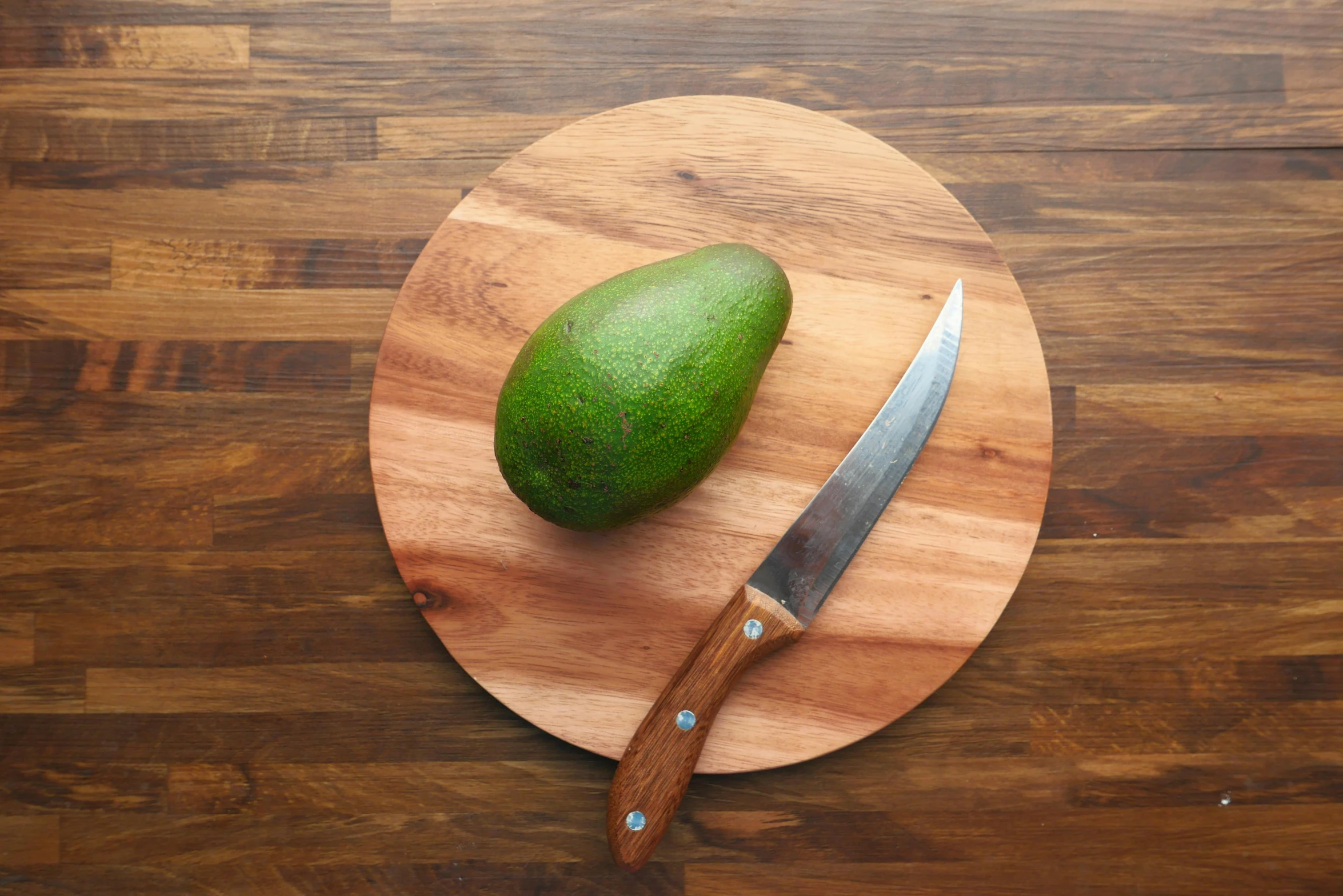 a knife sitting on top of a cutting board next to an avocado, by Matthias Stom, round-cropped, light wood, brown, flat