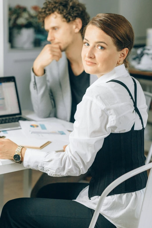 a man and a woman sitting at a table with a laptop, by Adam Marczyński, trending on pexels, renaissance, female in office dress, wearing a white blouse, cover shot, medium poly