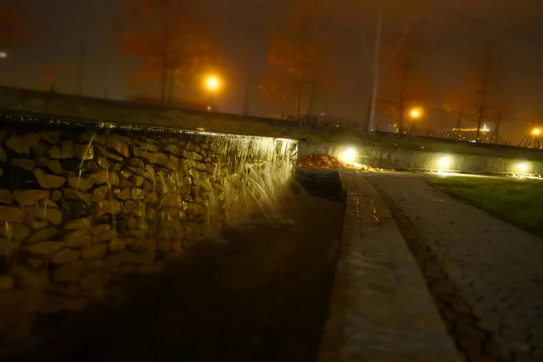 a man riding a skateboard down a sidewalk at night, by Muggur, small flowing stream from wall, storm drain, landscape architecture photo, vollumetric lighting