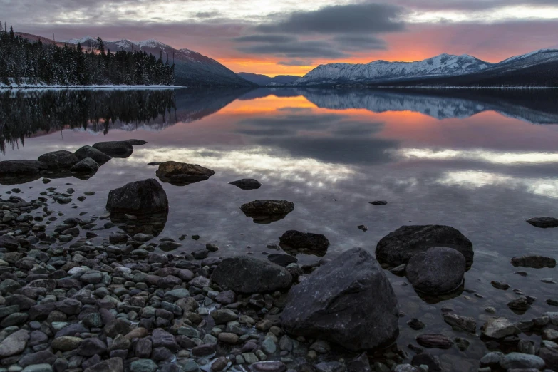 a large body of water surrounded by rocks, by Jim Nelson, pexels contest winner, hudson river school, mountain sunrise, winter lake setting, lava reflections, montana