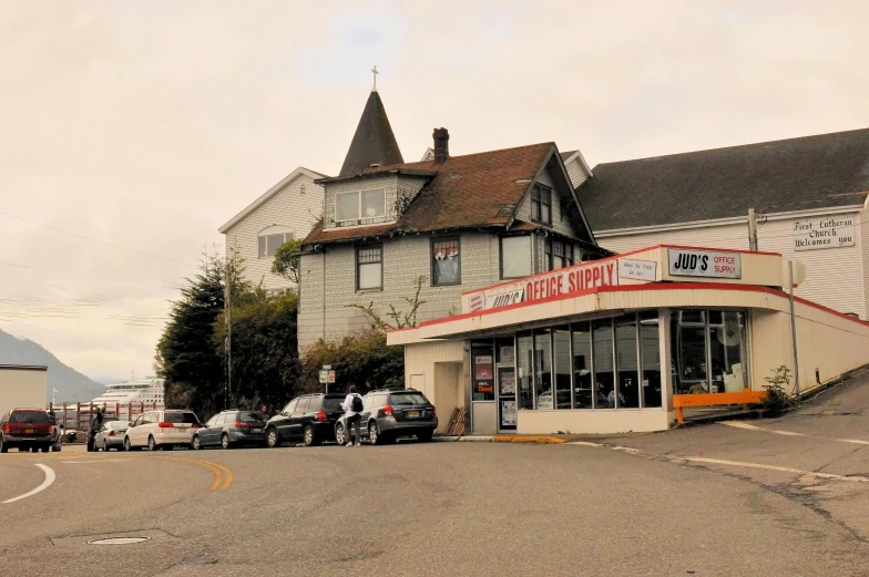 a group of cars parked in front of a building, a photo, by Jeffrey Smith, vancouver school, tillamook cheese, seaside victorian building, convenience store, view from a distance