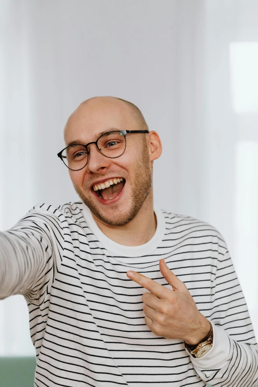 a man in a striped shirt holding a nintendo wii controller, a polaroid photo, inspired by Leo Leuppi, trending on pexels, antipodeans, portrait of bald, flirting smiling, jewish young man with glasses, selfie shot straight on angle