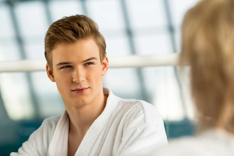 a man in a robe talking to a woman in a bathrobe, a picture, by Julian Allen, shutterstock, 1 7 - year - old boy thin face, long swept back blond hair, looking in mirror, lovingly looking at camera