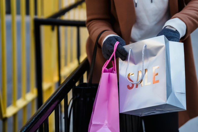 a close up of a person holding shopping bags, by Julia Pishtar, pexels contest winner, happening, square, wearing a pink hoodie, magazine sales, shop front