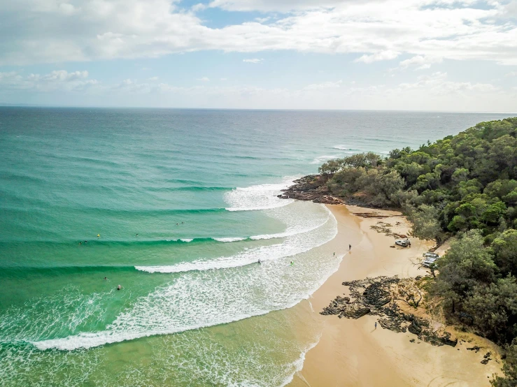 a large body of water next to a sandy beach, by Elizabeth Durack, pexels contest winner, drone footage, surfing, green waters, coastal cliffs