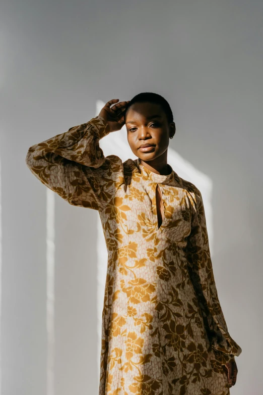 a woman standing in front of a white wall, trending on unsplash, renaissance, wearing yellow floral blouse, adut akech, beige and gold tones, soft silk dress