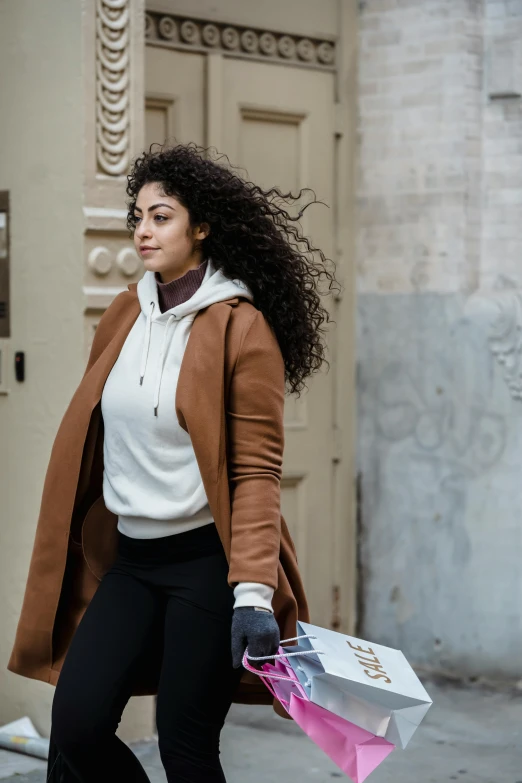 a woman walking down the street carrying shopping bags, a portrait, trending on pexels, renaissance, beige hoodie, black curly hair, marie - gabrielle capet style, young middle eastern woman