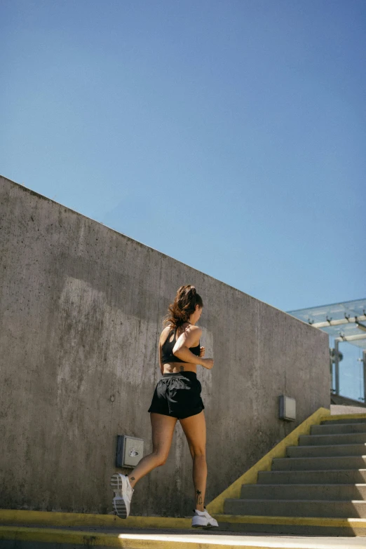 a woman running up a flight of stairs, unsplash, croptop and shorts, rooftop, sun overhead, on the concrete ground