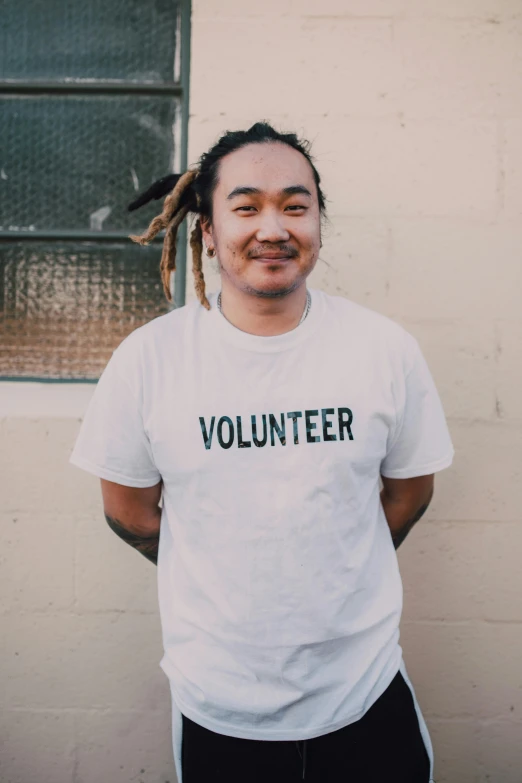 a man with dreadlocks standing in front of a building, inspired by Juan Villafuerte, trending on unsplash, printed on a cream linen t-shirt, joe taslim, slightly smiling, wearing white shirt