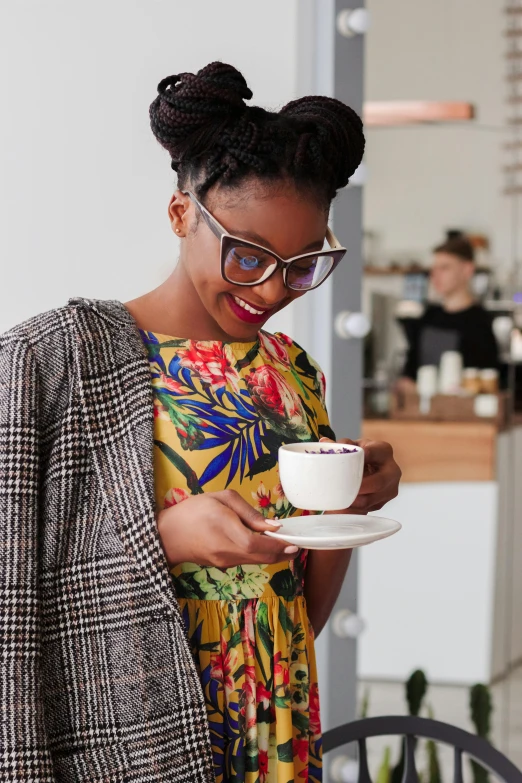 a woman in a colorful dress holding a cup of coffee, inspired by Richmond Barthé, dark skinned, small hipster coffee shop, wearing medium - sized glasses, curated collections