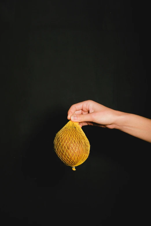 a person holding a piece of fruit in their hand, yellow translucent lace, standing with a black background, kete butcher, hegre