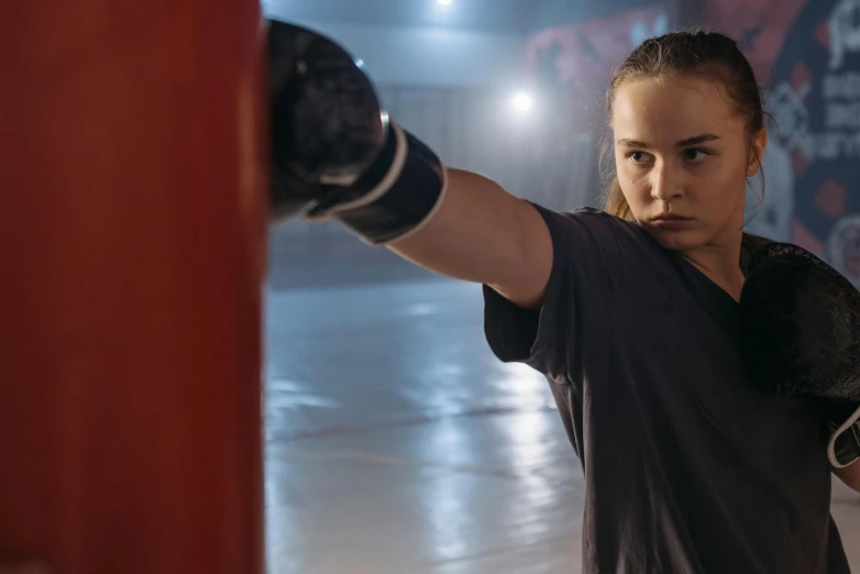 a woman standing next to a punching bag, a portrait, by Emma Andijewska, shutterstock, happening, joey king, fight scene, promotional image, aged 13