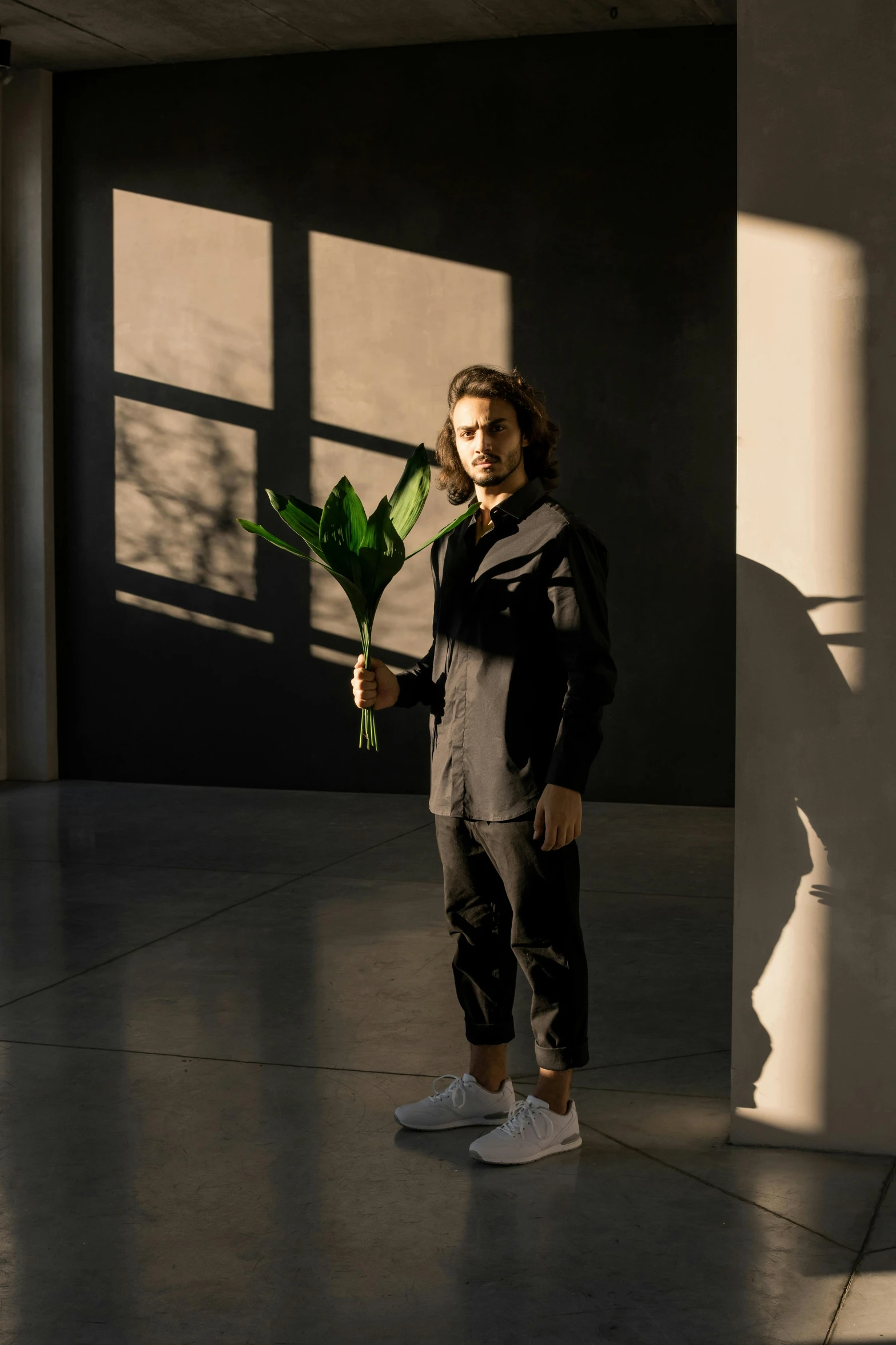a man standing in a room holding a plant, a portrait, unsplash, total black outfit, sun down, technical suit, architect