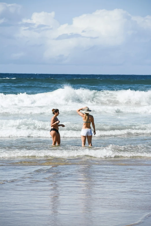 a couple of women standing on top of a beach next to the ocean, large waves, australian beach, hawaii beach, wearing a white bathing cap