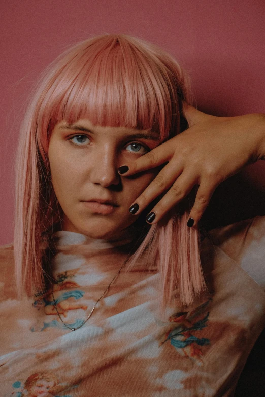 a woman with pink hair wearing a tie dye shirt, an album cover, inspired by Hannah Frank, trending on pexels, photorealism, with index finger, gold hair, sitting, ((pink))