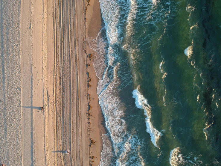 a group of people standing on top of a beach next to the ocean, by Niko Henrichon, pexels contest winner, bird\'s eye view, new jersey, rippling oceanic waves, thumbnail