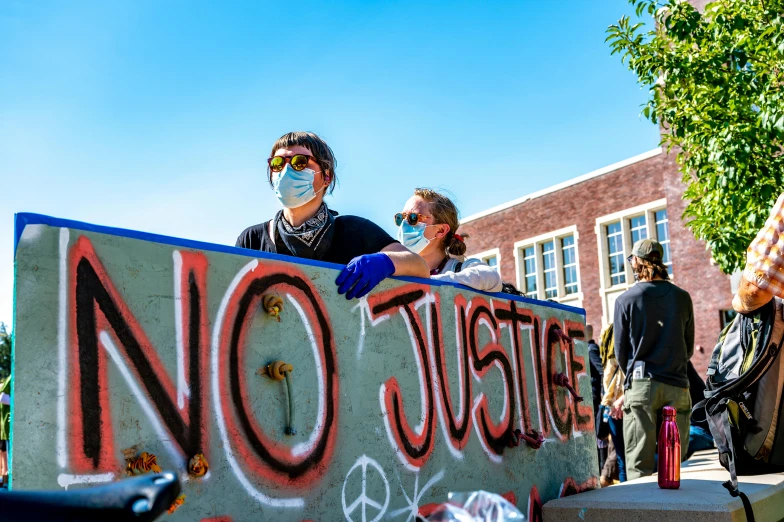 a group of people holding a sign that says no justice, a photo, by Washington Allston, unsplash, graffiti, wearing facemask and sunglasses, avatar image, high school, hanging