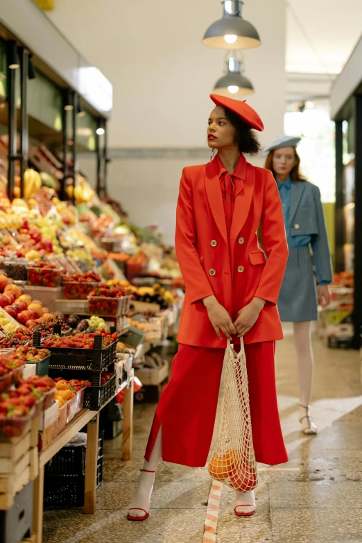 a woman in a red coat is standing in a market, a digital rendering, trending on pexels, mango, red suit, wearing a french beret, lookbook