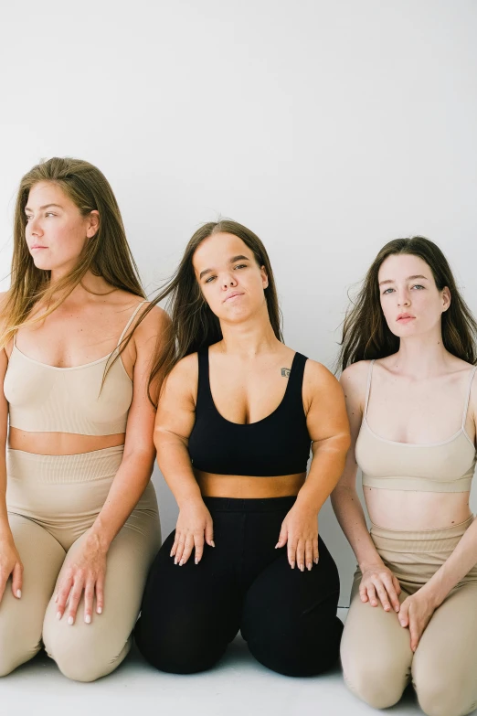 a group of women sitting next to each other, an album cover, inspired by Vanessa Beecroft, trending on unsplash, sports bra, seamless, natural muted tones, 3 - piece